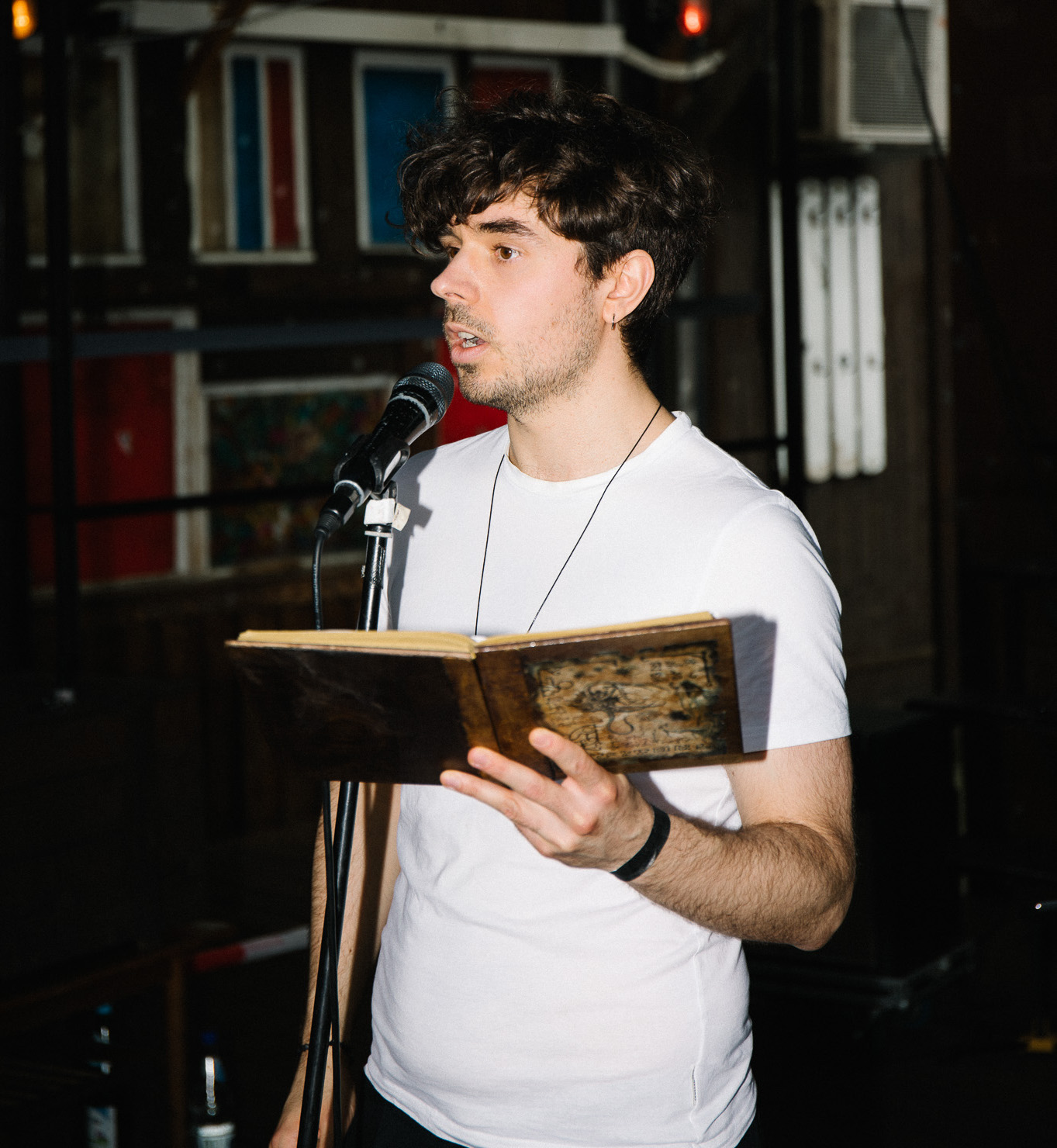 A persone speaking to an audience trough the microphone with a book in his hands