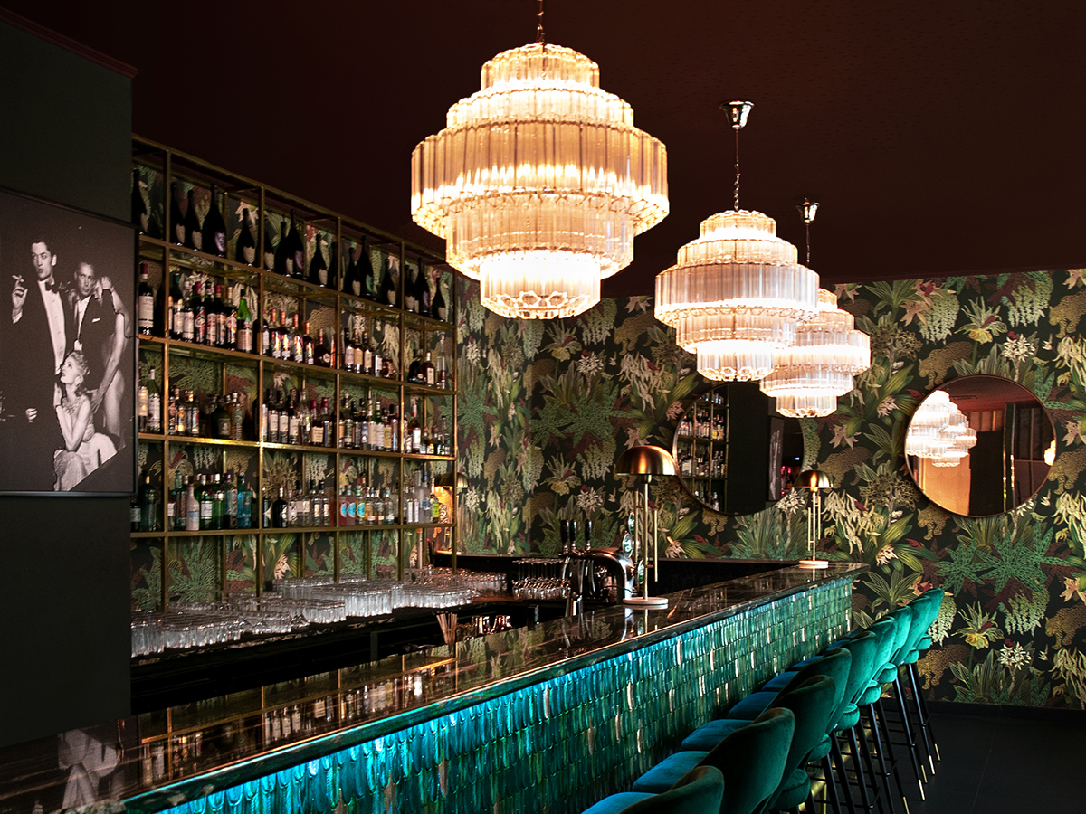 Backside of a bar with bottles and Chandeliers in front.