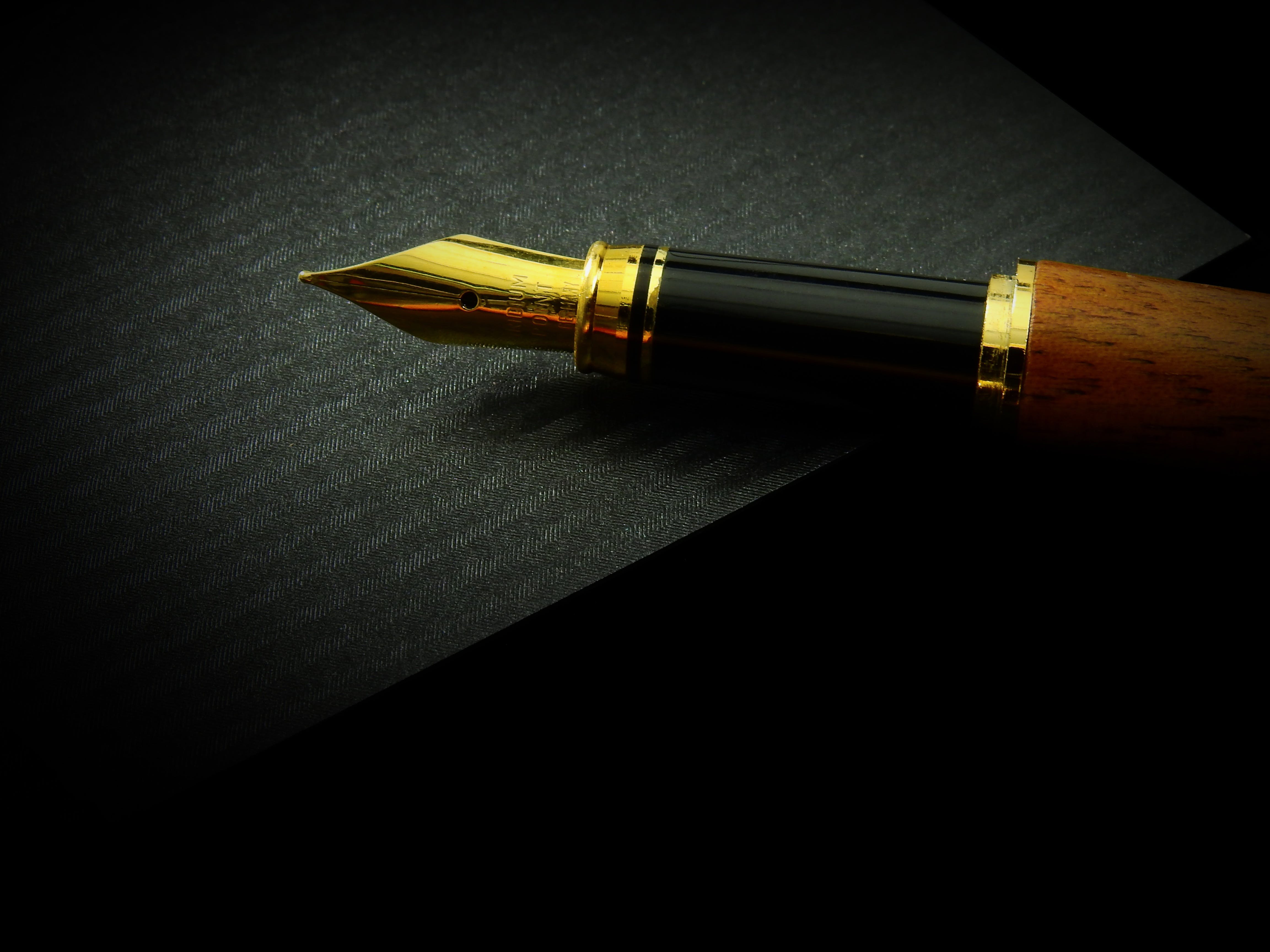 A vintage ink pen lying on a dark table with low-light background.